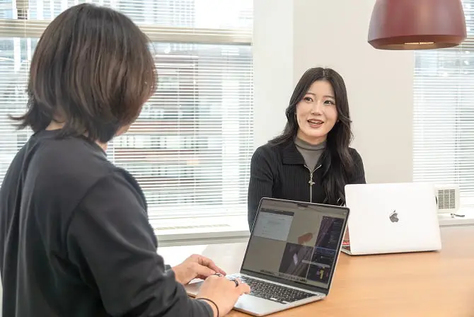 テーブルを挟んでノートパソコンを見ながら話し合う2人のビジネスパーソン