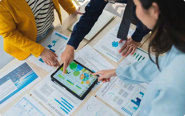 タブレットと書類を囲んでデータを検討する3人のビジネスパーソン