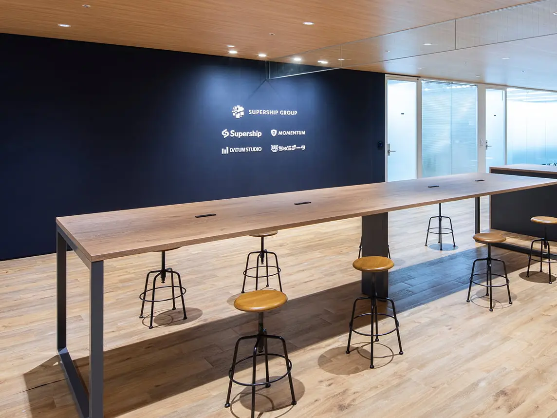 MOMENTUM GROUPのロゴが描かれたアクセントウォールとコミュニティテーブルがある明るいオフィス環境
