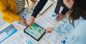 テーブル上のタブレットと書類を囲んでデータを検討するビジネスパーソン