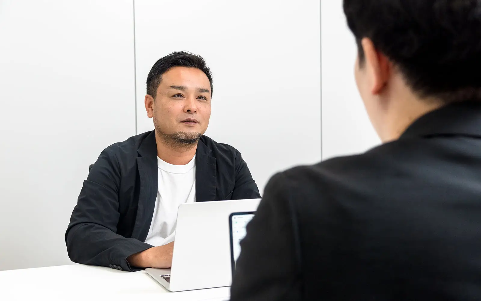 ノートパソコンを置いたテーブルで向かい合って話し合うビジネスパーソン