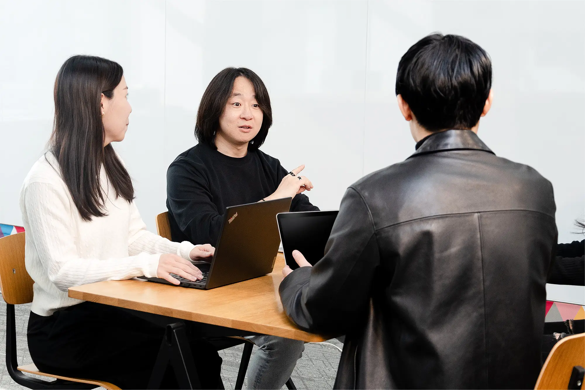 会議テーブルでノートパソコンとタブレットを使いながら話し合う3人のビジネスパーソン